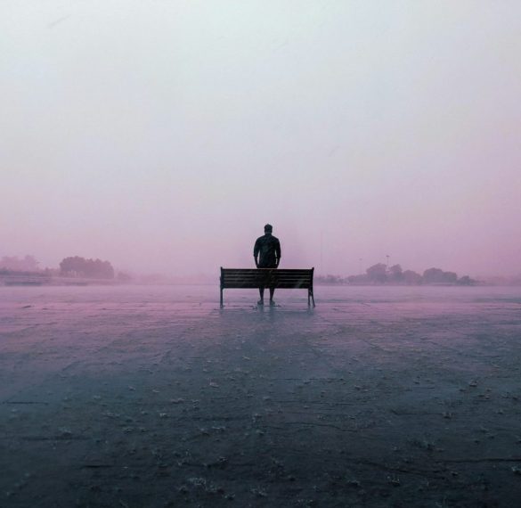 Misty scene with a person’s silhouette beside a bench in soft pink fog
